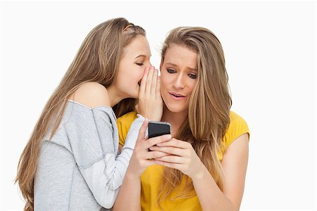 Student whispering to her friend who's texting on her phone against white background Stock Photo - Budget Royalty-Free & Subscription, Code: 400-06637941