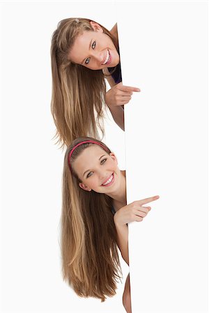 Portrait of two long hair students pointing behind a blank sign against white background Stock Photo - Budget Royalty-Free & Subscription, Code: 400-06638096
