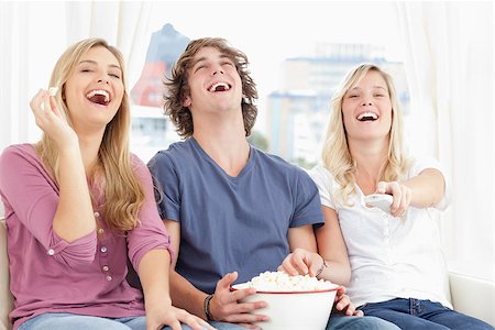 Three friends eating popcorn while laughing at the show while they sit on the couch together Stock Photo - Budget Royalty-Free & Subscription, Code: 400-06638240