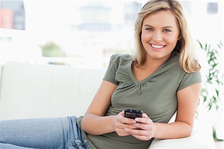 A woman lying on the couch smiles as she uses her phone while looking forward. Stock Photo - Budget Royalty-Free & Subscription, Code: 400-06632919