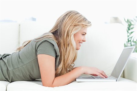 A woman lying across the couch smiles as she uses her laptop. Stock Photo - Budget Royalty-Free & Subscription, Code: 400-06632978