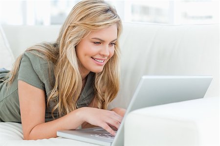 A woman smiling as she uses her laptop while lying across the couch. Stock Photo - Budget Royalty-Free & Subscription, Code: 400-06632970