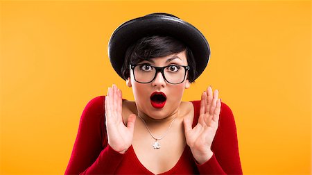 Beautiful girl with a astonished expression, wearing a hat and nerd glasses over a yellow background Stock Photo - Budget Royalty-Free & Subscription, Code: 400-06633450