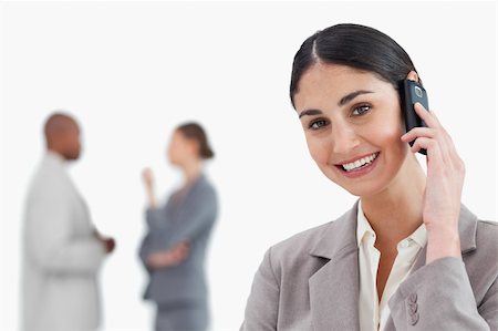 simsearch:400-06686555,k - Smiling saleswoman with mobile phone and colleagues behind her against a white background Stock Photo - Budget Royalty-Free & Subscription, Code: 400-06685321