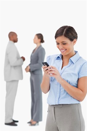 simsearch:400-06686562,k - Businesswoman looking at cellphone with associates behind her against a white background Foto de stock - Super Valor sin royalties y Suscripción, Código: 400-06685352