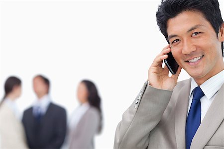 simsearch:400-06686555,k - Smiling businessman on mobile phone and team behind him against a white background Stock Photo - Budget Royalty-Free & Subscription, Code: 400-06686557