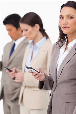 simsearch:400-06686555,k - Businesswoman with cellphone next to colleagues against a white background Stock Photo - Budget Royalty-Free & Subscription, Code: 400-06686550