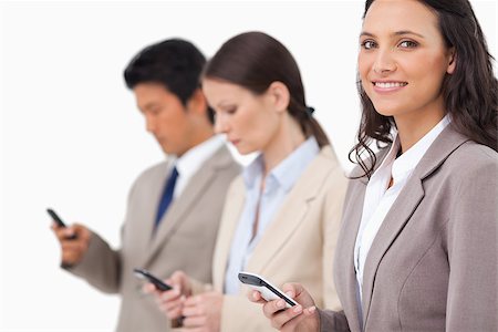 simsearch:400-06686555,k - Smiling saleswoman with cellphone next to colleagues against a white background Stock Photo - Budget Royalty-Free & Subscription, Code: 400-06686551