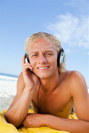 Young blonde man attentively listening to music while lying on then beach Stock Photo - Budget Royalty-Free & Subscription, Code: 400-06687004