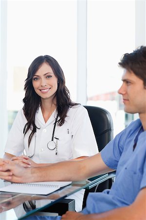 Enthusiastic female doctor sitting at the desk while looking at the camera near a co-worker Stock Photo - Budget Royalty-Free & Subscription, Code: 400-06688608