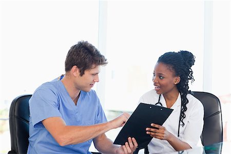 Young serious doctor showing something on a clipboard to his smiling co-worker Stock Photo - Budget Royalty-Free & Subscription, Code: 400-06688617