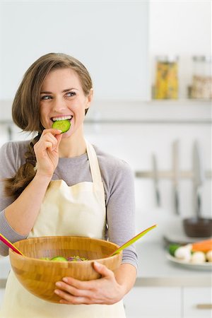 Happy young housewife tasting slice of cucumber from vegetable salad Stock Photo - Budget Royalty-Free & Subscription, Code: 400-06697849