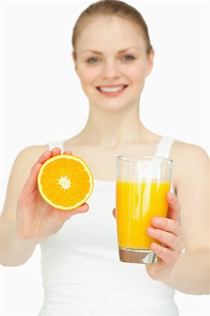 simsearch:400-06689686,k - Smiling woman presenting an orange while holding a glass against white background Foto de stock - Super Valor sin royalties y Suscripción, Código: 400-06690082
