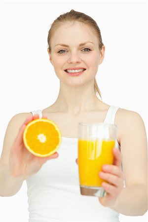 simsearch:400-06689686,k - Smiling woman holding a glass while presenting an orange against white background Foto de stock - Super Valor sin royalties y Suscripción, Código: 400-06690083