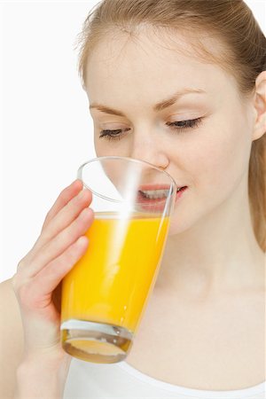 simsearch:400-06689686,k - Woman drinking a glass of orange juice while looking at it against white background Foto de stock - Super Valor sin royalties y Suscripción, Código: 400-06690103