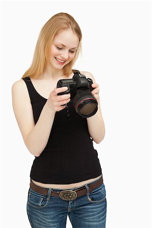 people holding camera slr - Woman looking at the screen of her camera while smiling against white background Stock Photo - Budget Royalty-Free & Subscription, Code: 400-06690295