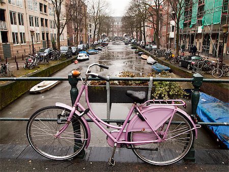 A pink bicycle locked to a railing on a bridge over a canal in Amsterdam. Bikes are a dominant form of transportation in the Netherlands. Stockbilder - Microstock & Abonnement, Bildnummer: 400-06693168