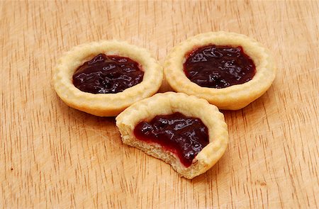 simsearch:400-06693299,k - Three yummy jam tarts, one with a bite taken from it, on a wooden table Foto de stock - Royalty-Free Super Valor e Assinatura, Número: 400-06693301