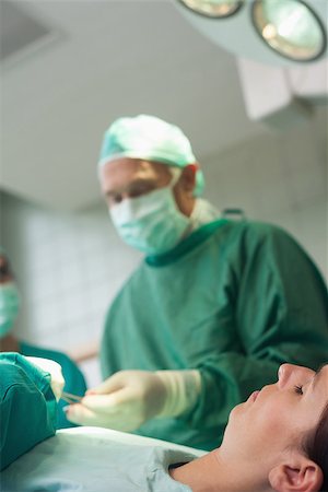 Patient sleeping on a surgical table while a surgeon is taking scissors in a surgical room Stock Photo - Budget Royalty-Free & Subscription, Code: 400-06734064