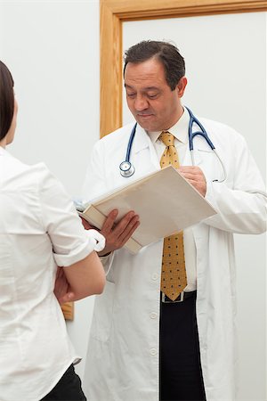 Doctor looking into a file while talking to a woman in a hallway Stock Photo - Budget Royalty-Free & Subscription, Code: 400-06734137