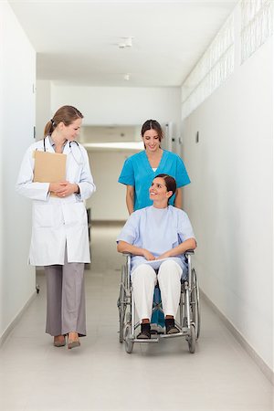 simsearch:400-06875952,k - Nurse pushing a patient in a wheelchair while talking to a doctor in a hospital hallway Stockbilder - Microstock & Abonnement, Bildnummer: 400-06734232