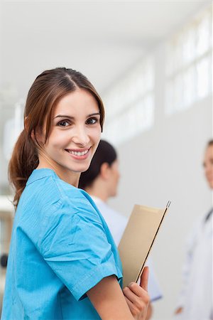 simsearch:400-06734741,k - Nurse smiling while holding files and standing with a doctor and a patient in a hallway Photographie de stock - Aubaine LD & Abonnement, Code: 400-06734244