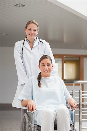 simsearch:6109-06195982,k - Smiling doctor next to a patient on a wheelchair in hospital corridor Fotografie stock - Microstock e Abbonamento, Codice: 400-06734676