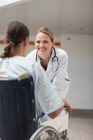 simsearch:6109-06195982,k - Doctor looking at a female patient on a wheelchair in hospital hallway Fotografie stock - Microstock e Abbonamento, Codice: 400-06734682