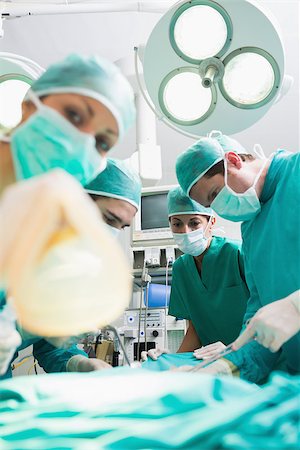 simsearch:400-06735487,k - Nurse holding an oxygen mask next to surgeons in an operating theatre Fotografie stock - Microstock e Abbonamento, Codice: 400-06735487