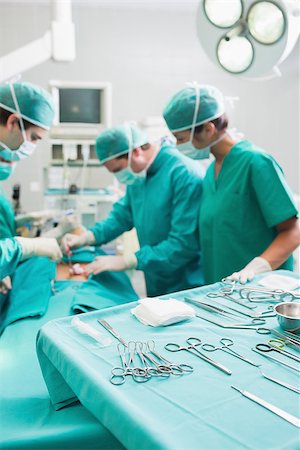 simsearch:400-06735487,k - Surgical tools on a surgical tray while surgeons are operating in a hospital Fotografie stock - Microstock e Abbonamento, Codice: 400-06735549