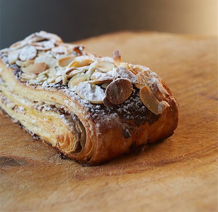 Fresh chocolate and Almond rollover croissant pastry, sprinkled with icing sugar on a brown wooden serving board with copy space  - Shallow Depth of Field (DOF) Stock Photo - Budget Royalty-Free & Subscription, Code: 400-06739257