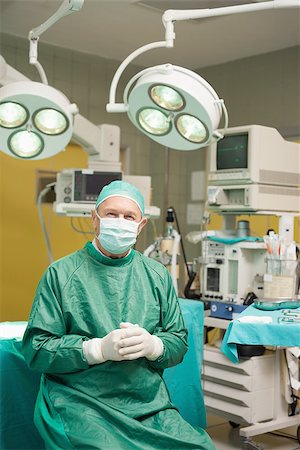 simsearch:400-06734621,k - Smiling surgeon sitting while joining his hands together in a surgical room Stock Photo - Budget Royalty-Free & Subscription, Code: 400-06733973