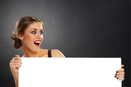Excited joyful young woman holding blank white billboard against dark background. Stock Photo - Budget Royalty-Free & Subscription, Code: 400-06746365