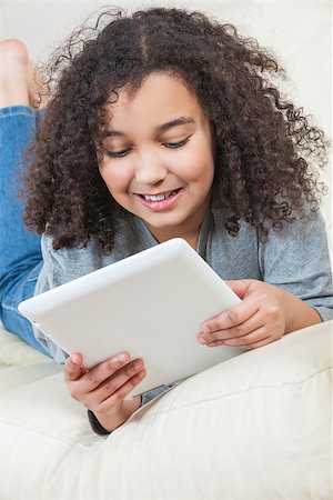 Beautiful happy young mixed race African American girl smiling and using a tablet computer at home on her sofa Stock Photo - Budget Royalty-Free & Subscription, Code: 400-06752050