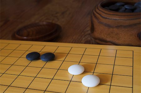 A set of the traditional Asian board game go. A bowl with black stones is in the background. Shallow depth of field. Stockbilder - Microstock & Abonnement, Bildnummer: 400-06763692