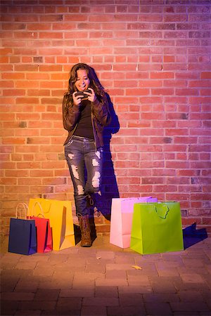 Pretty Mixed Race Young Adult Woman with Shopping Bags Using Her Cell Phone Against a Brick Wall - Plenty of Copy Space. Stock Photo - Budget Royalty-Free & Subscription, Code: 400-06797826
