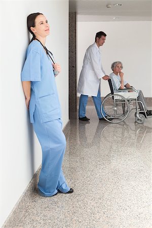 simsearch:400-07337135,k - Nurse leaning against wall with doctor pushing patient in wheelchair Stock Photo - Budget Royalty-Free & Subscription, Code: 400-06799525