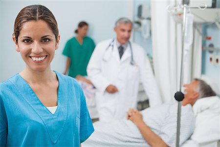 Happy nurse in hospital room with doctor, patient and other nurse in background Stock Photo - Budget Royalty-Free & Subscription, Code: 400-06799606