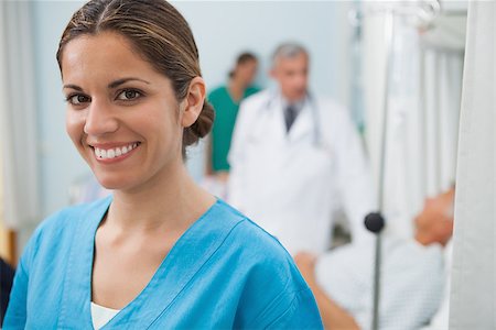 Smiling nurse in hospital room with doctor, patient and other nurse in background Stock Photo - Budget Royalty-Free & Subscription, Code: 400-06799608
