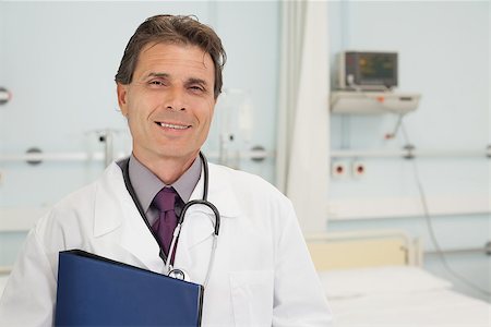 simsearch:400-06799599,k - Smiling doctor holding a folder in hospital bedroom Foto de stock - Super Valor sin royalties y Suscripción, Código: 400-06799601