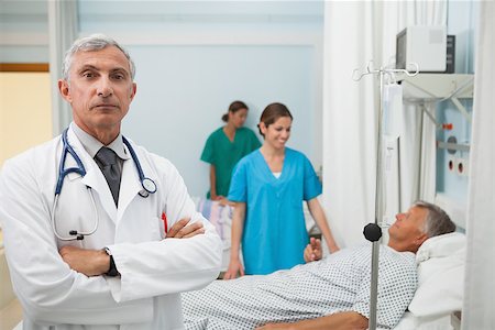 Doctor with folded arms in hospital room with two nurses and a patient in the background Stock Photo - Budget Royalty-Free & Subscription, Code: 400-06799611