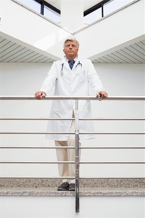 simsearch:400-06799599,k - Thinking doctor stands at railing looking up in hospital corridor Foto de stock - Super Valor sin royalties y Suscripción, Código: 400-06799639