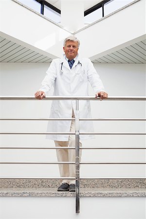 Smiling doctor in lab coat leaning against rail in hospital corridor Stock Photo - Budget Royalty-Free & Subscription, Code: 400-06799649