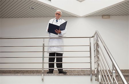 Doctor reading patient files leaning against railing in hospital corridor Stock Photo - Budget Royalty-Free & Subscription, Code: 400-06799668
