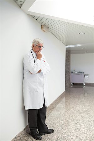 simsearch:400-07334526,k - Thinking doctor leaning against wall with hand holding chin in hospital corridor Stockbilder - Microstock & Abonnement, Bildnummer: 400-06799681
