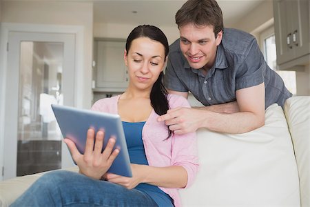 Woman sitting on the couch and uses a tablet computer with her man behind her Stock Photo - Budget Royalty-Free & Subscription, Code: 400-06800271
