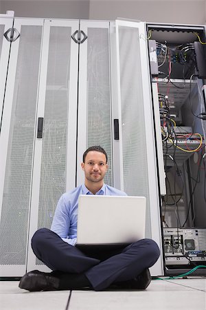 simsearch:400-06801216,k - Man sitting in front of servers with his laptop on the floor of data center Foto de stock - Royalty-Free Super Valor e Assinatura, Número: 400-06801335