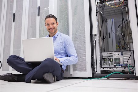 simsearch:400-06801216,k - Smiling man sitting on floor checking servers with laptop in data center Foto de stock - Royalty-Free Super Valor e Assinatura, Número: 400-06801331