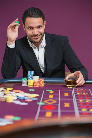 simsearch:400-06802094,k - Man holding a chip and a glass of whiskey sitting at roulette table Foto de stock - Super Valor sin royalties y Suscripción, Código: 400-06801952