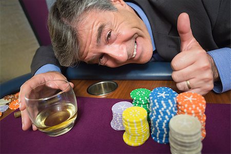 simsearch:400-06802094,k - Man leaning on table with whiskey glass giving thumbs up in casino Foto de stock - Super Valor sin royalties y Suscripción, Código: 400-06801970